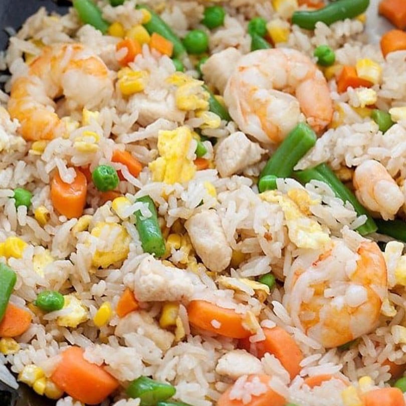 Close-up of fried rice with shrimp, chicken, carrots, peas, corn, and scrambled egg.