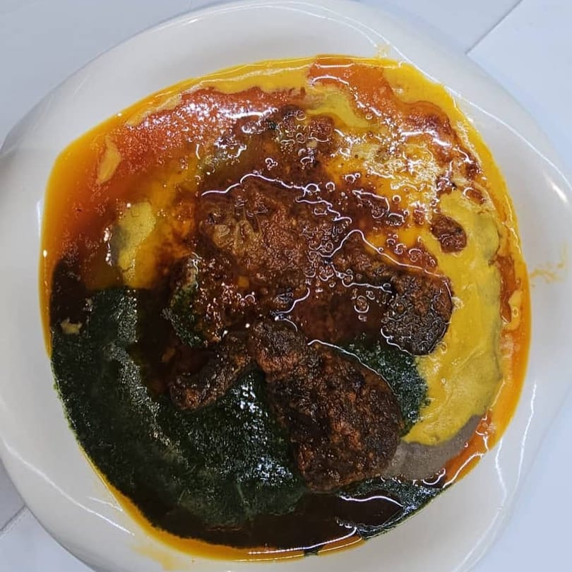 A vibrant African dish with yellow, orange, and dark green sections, topped with brown meat.