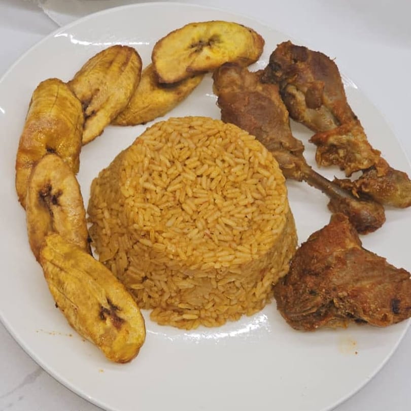 African jollof rice, fried plantains, and crispy fried chicken on a white plate.